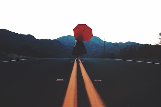 woman walking in the middle of the road with umbrella during day in Arizona United States