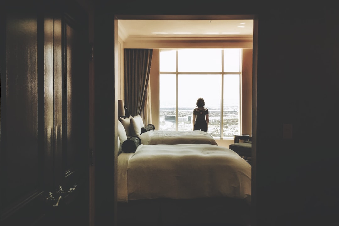  woman standing near window inside bedroom double bed