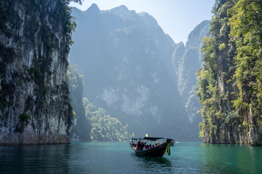 A longtail boat crossing Cheow Lan lake beneath limestone cliffs in Khao Sok