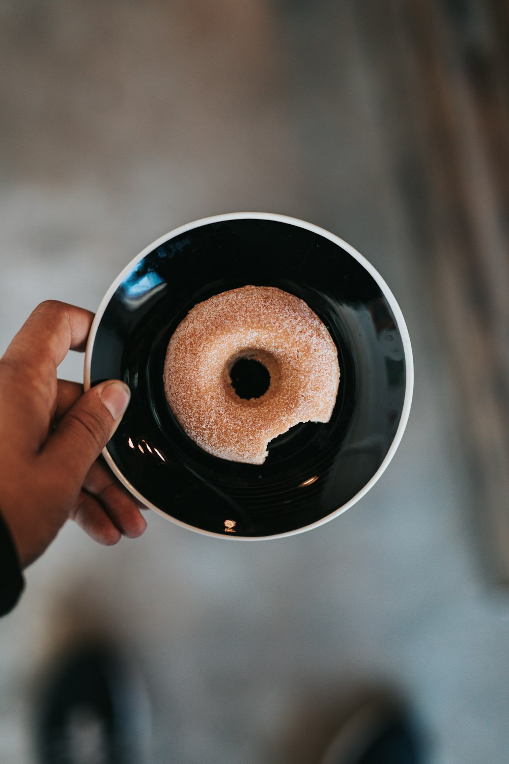 person holding black ceramic plate with donut