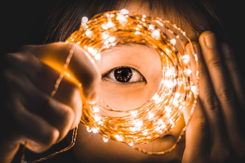 person covering one eye while holding yellow string lights
