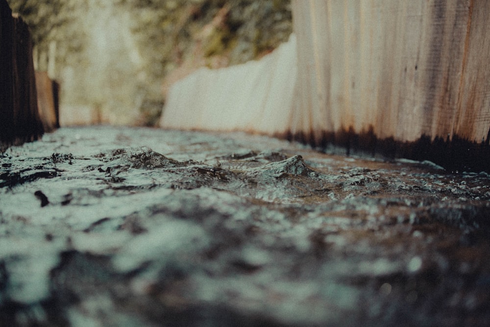 um fluxo de água correndo por uma rua ao lado de uma cerca de madeira