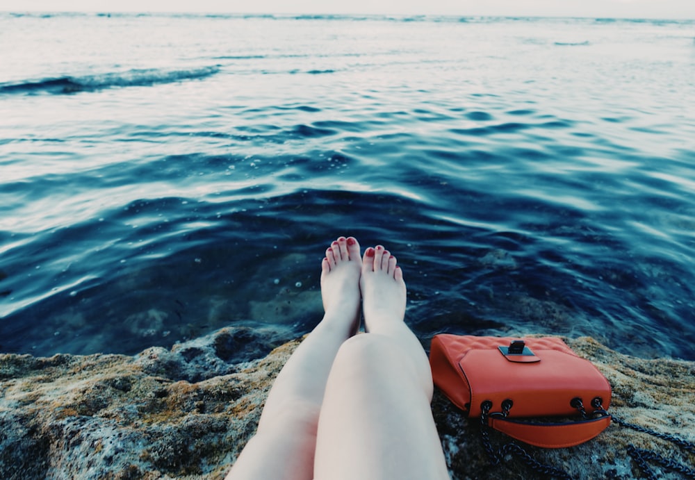 person sitting near rock beside body of water