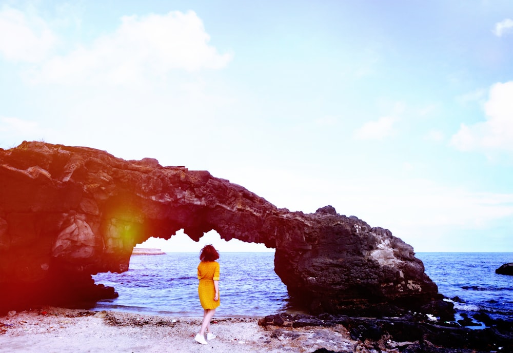 woman standing below arch on sea