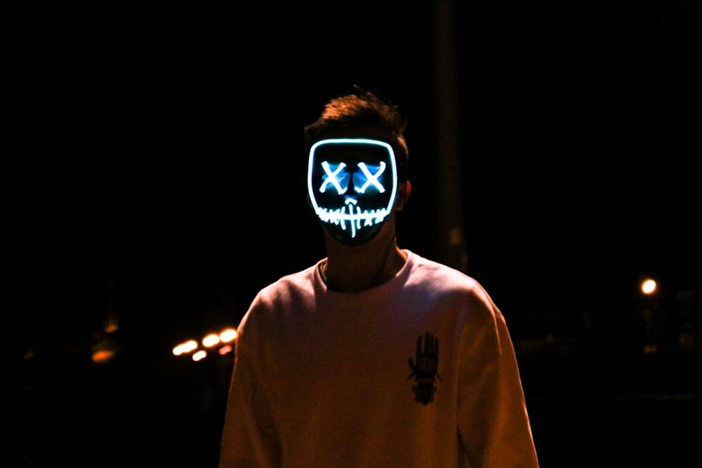 man standing in the dark wearing lighted stitched mouth and crossed eyes mask