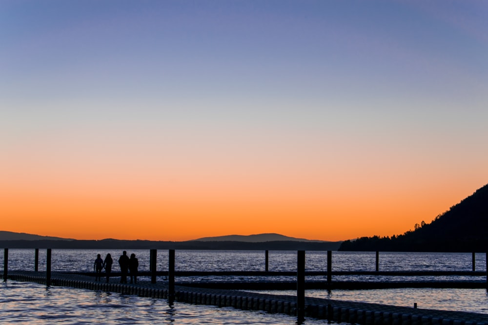 silhouette of people walking along footbridge above sea during golden hour