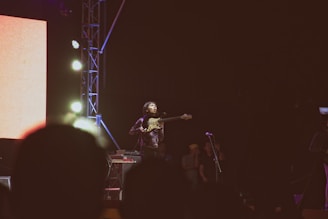 A kora player passionately performing on stage with a vibrant audience in the background.