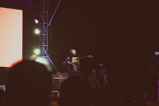 A kora player passionately performing on stage with a vibrant audience in the background.