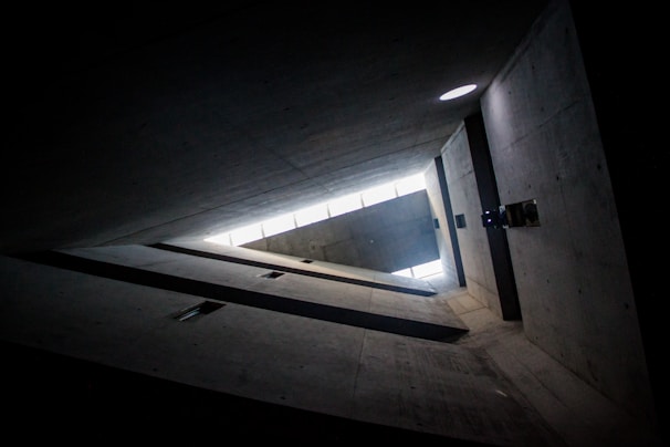 Interior shot of a minimalist brutalist space with natural light filtering through narrow windows and concrete surfaces.