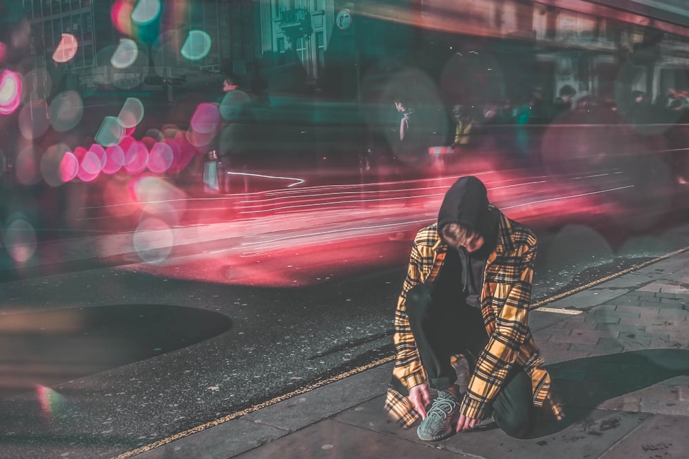 man lacing shoes beside street timelapse photography