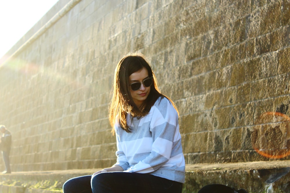 woman sitting beside brown concrete wall