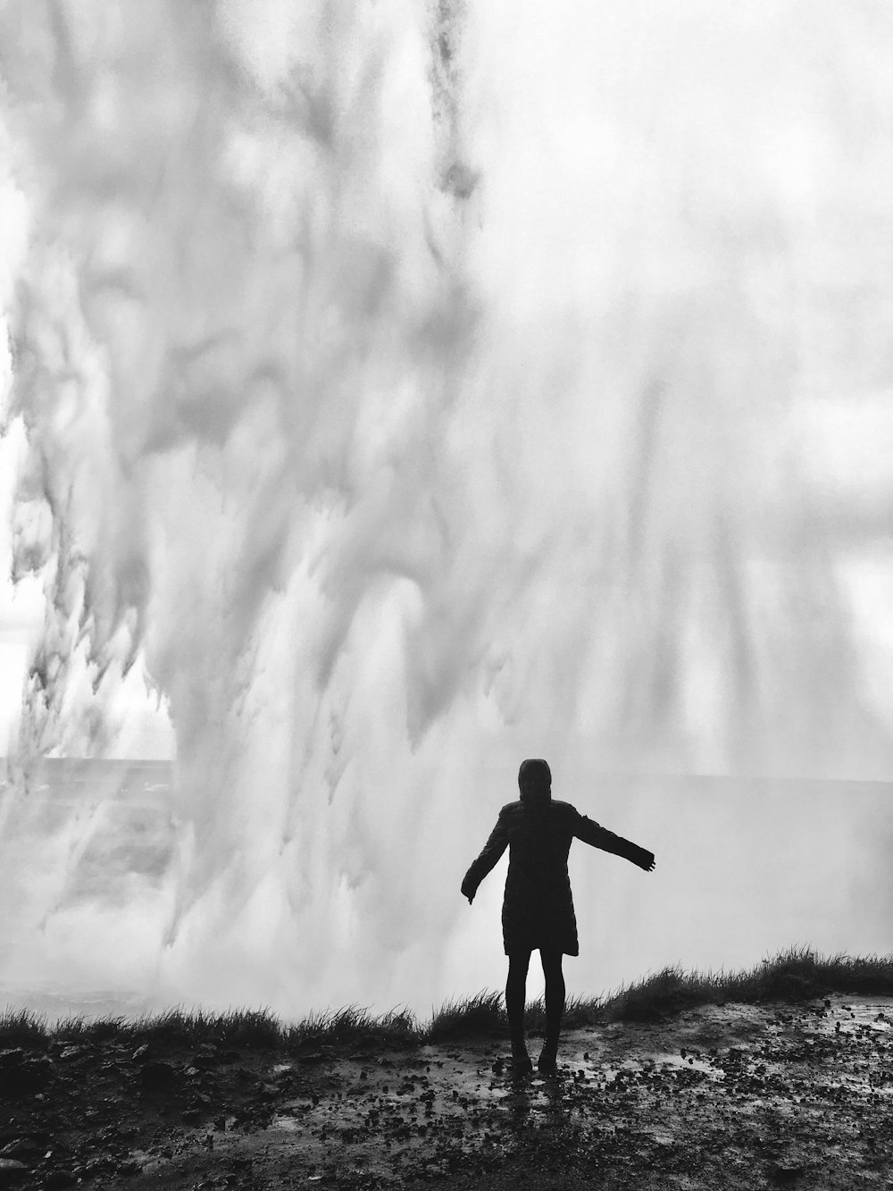 fotografia em tons de cinza de uma pessoa em pé na frente de respingos de ondas de água