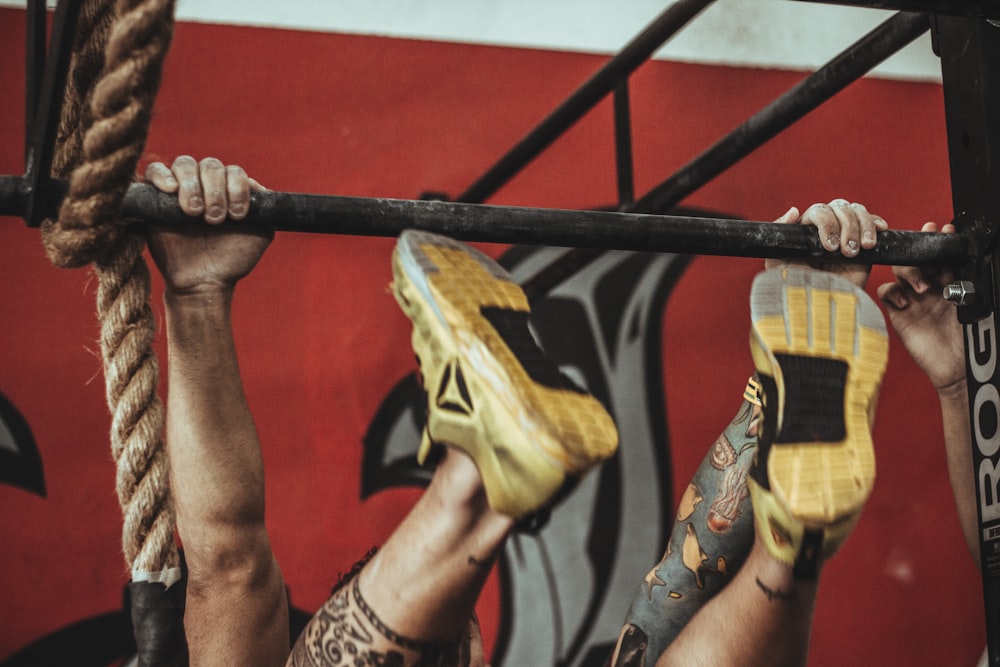 pessoa vestindo sapatos esportivos de cano baixo amarelo e preto Reebok pendurados na barra pull-up