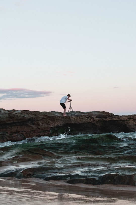 man standing on rock holding camera near body of water in Newcastle Australia
