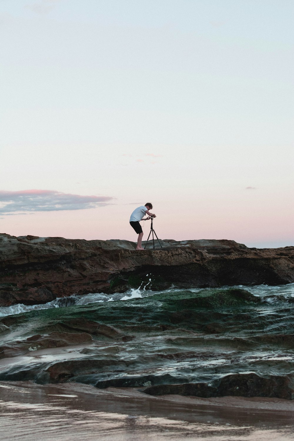 man standing on rock holding camera near body of water