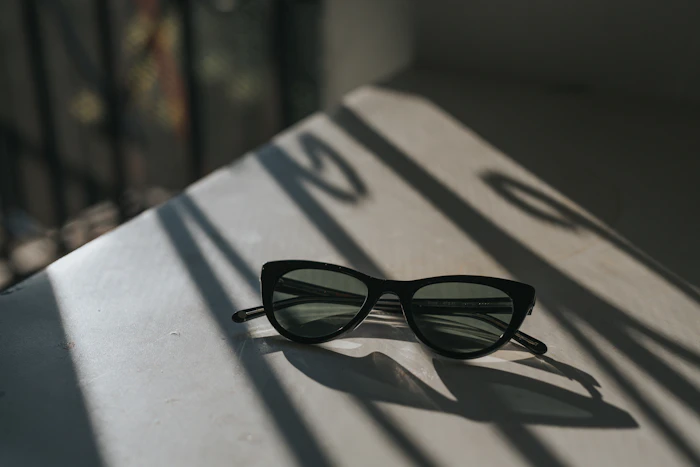 Black sunglasses on a sunlit table with striped window shadows (stand-in for the eye area)