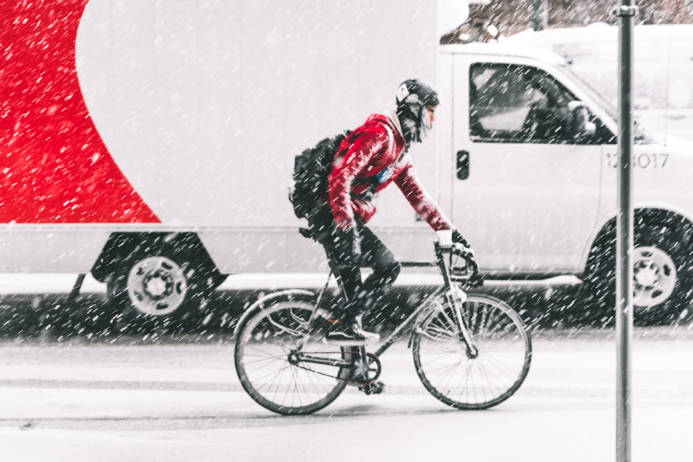 persona con chaqueta roja montando en bicicleta de montaña con un vehículo blanco cerca durante el invierno
