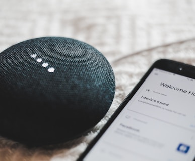 turned-on charcoal Google Home Mini and smartphone