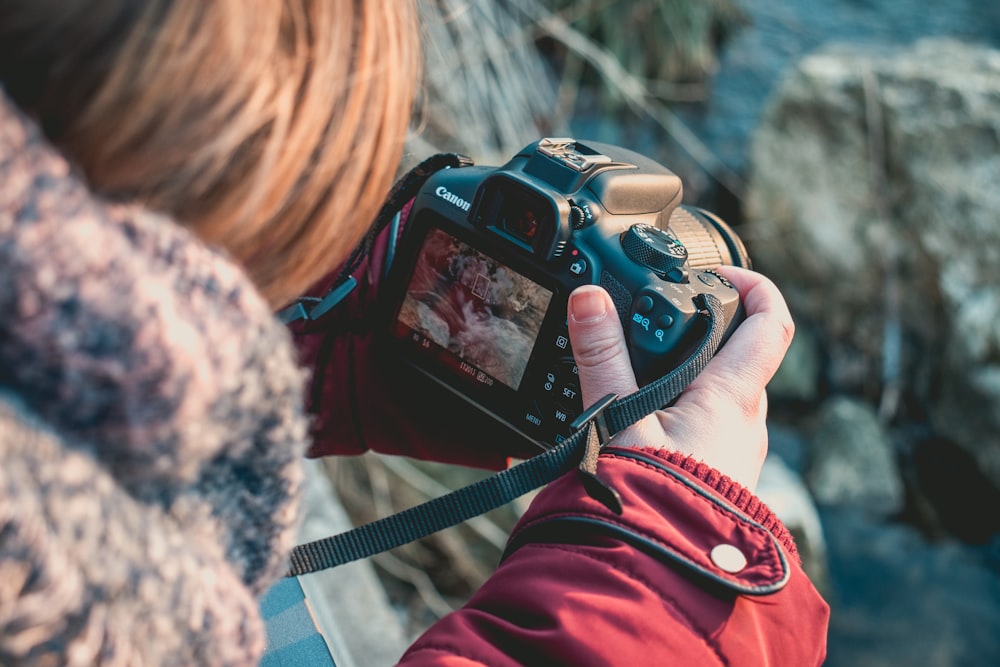 검은색 캐논 DSLR 카메라를 사용하는 사람의 얕은 초점 촬영