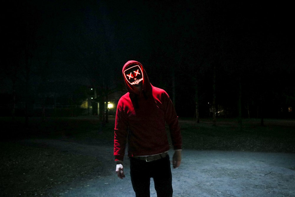 person in red pullover hooded jacket standing in street during nighttime