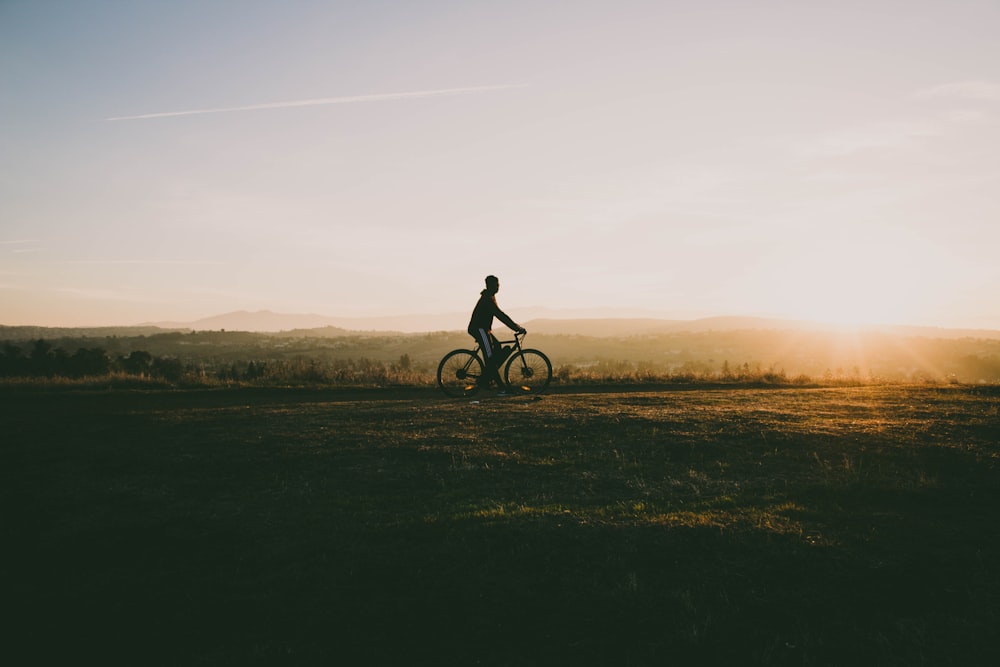 person riding bicycle near grass in sunset