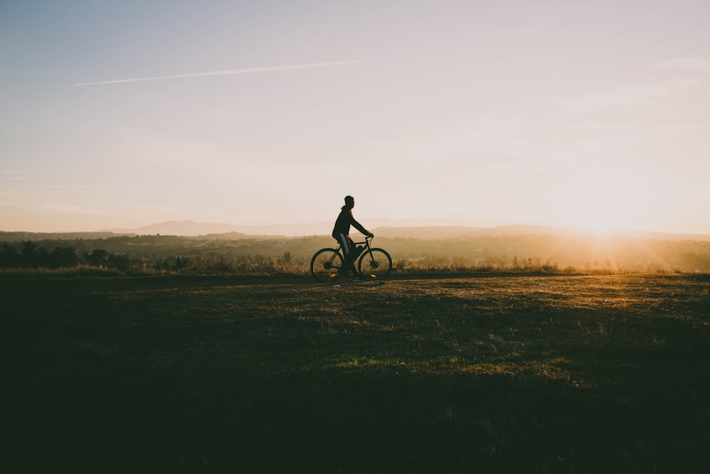 Person, die Fahrrad in der Nähe von Gras bei Sonnenuntergang fährt
