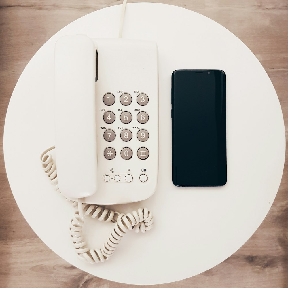 white home telephone beside black Android smartphone