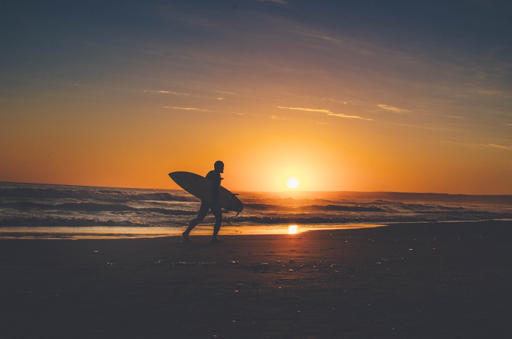 silhouette of person holding surfboard near body of water