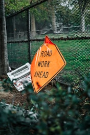 road work ahead signage leaning on chain link fence