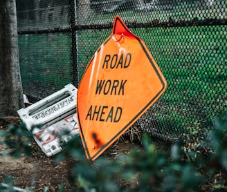 road work ahead signage leaning on chain link fence