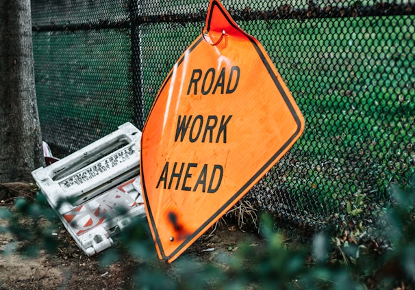 road work ahead signage leaning on chain link fence