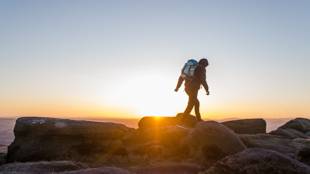 silhouette of man carrying backpack walking on stones