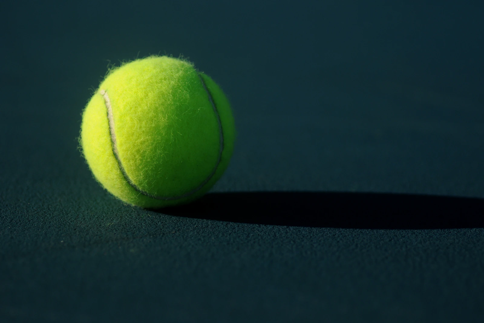 Plain yellow tennis ball on a dark court