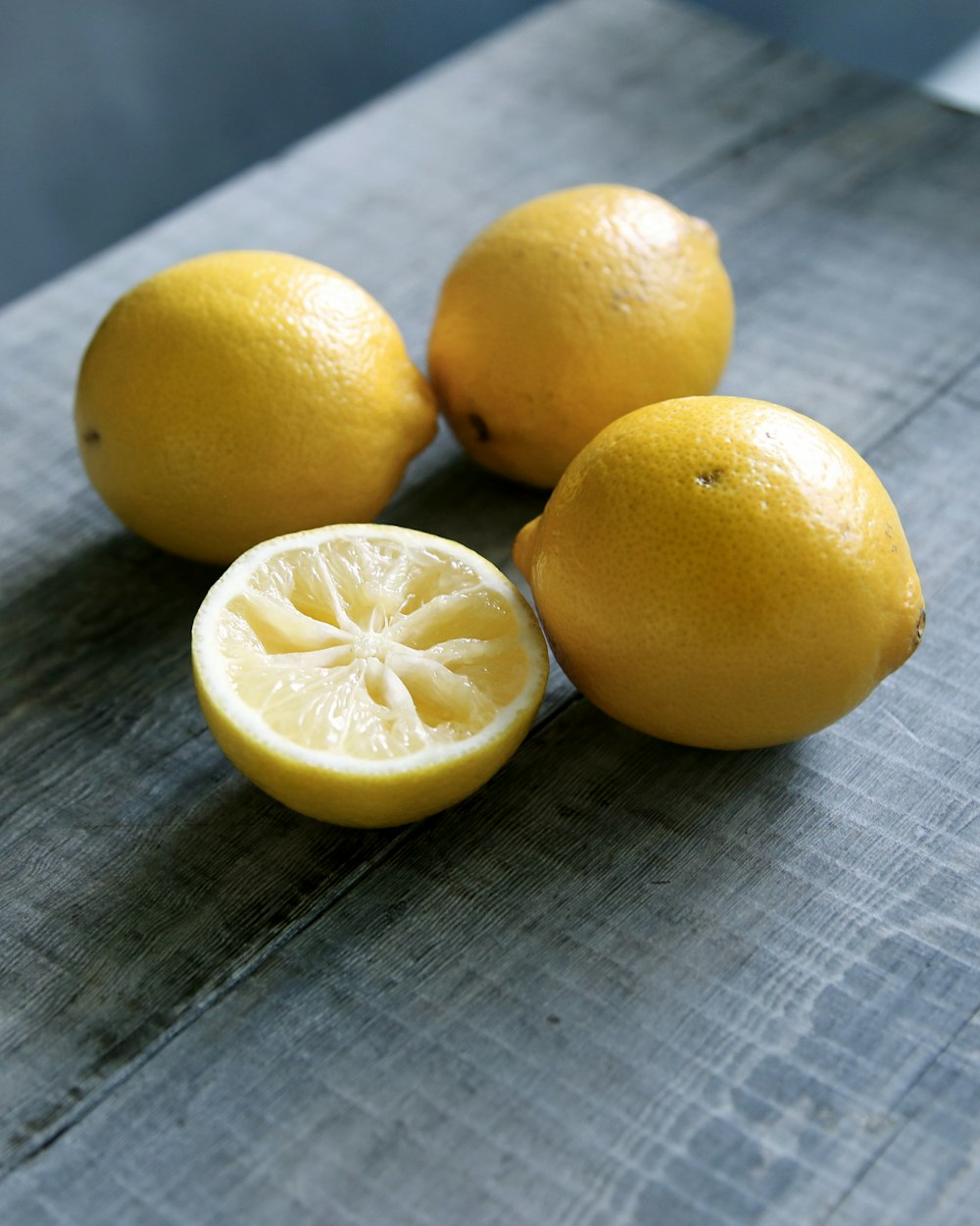 três limões amarelos ao lado de limão fatiado colocado na superfície de madeira cinza