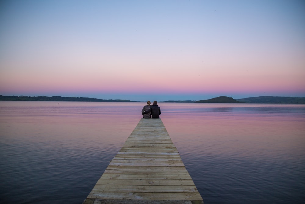 Dos personas sentadas en el muelle del océano