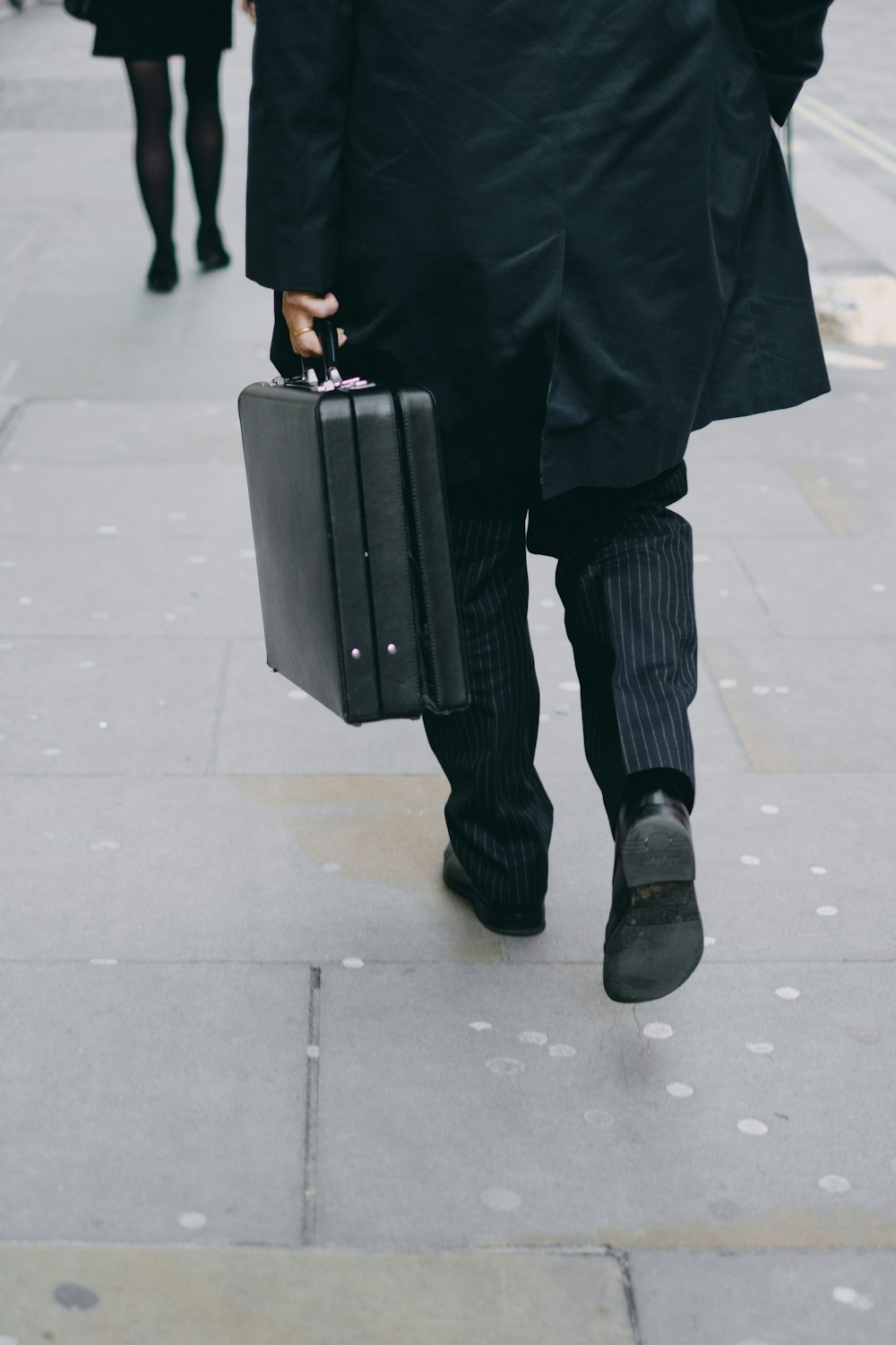 person carrying suit case while walking on pavement