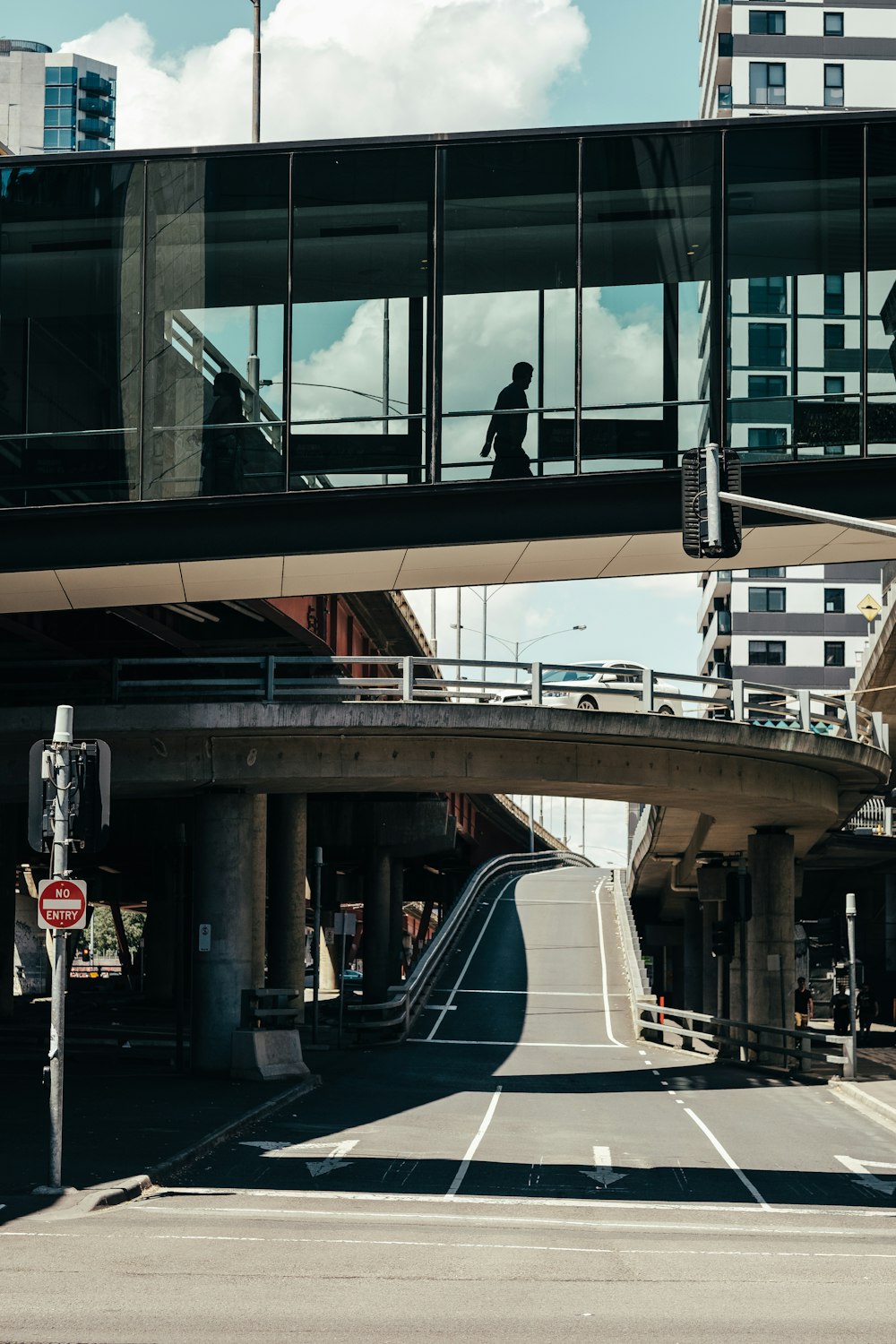 uomo che cammina sul ponte con tetto di vetro vicino a una strada di cemento grigia durante il giorno
