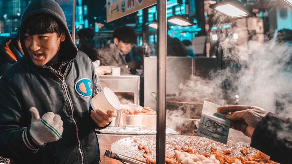 man holding disposable cup standing beside food cart