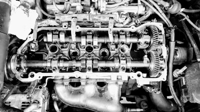 An exposed engine cylinder head displays mechanical components such as camshafts, gears, and valves. The intricate arrangement of parts highlights the complexity of engine design.