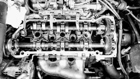 An exposed engine cylinder head displays mechanical components such as camshafts, gears, and valves. The intricate arrangement of parts highlights the complexity of engine design.