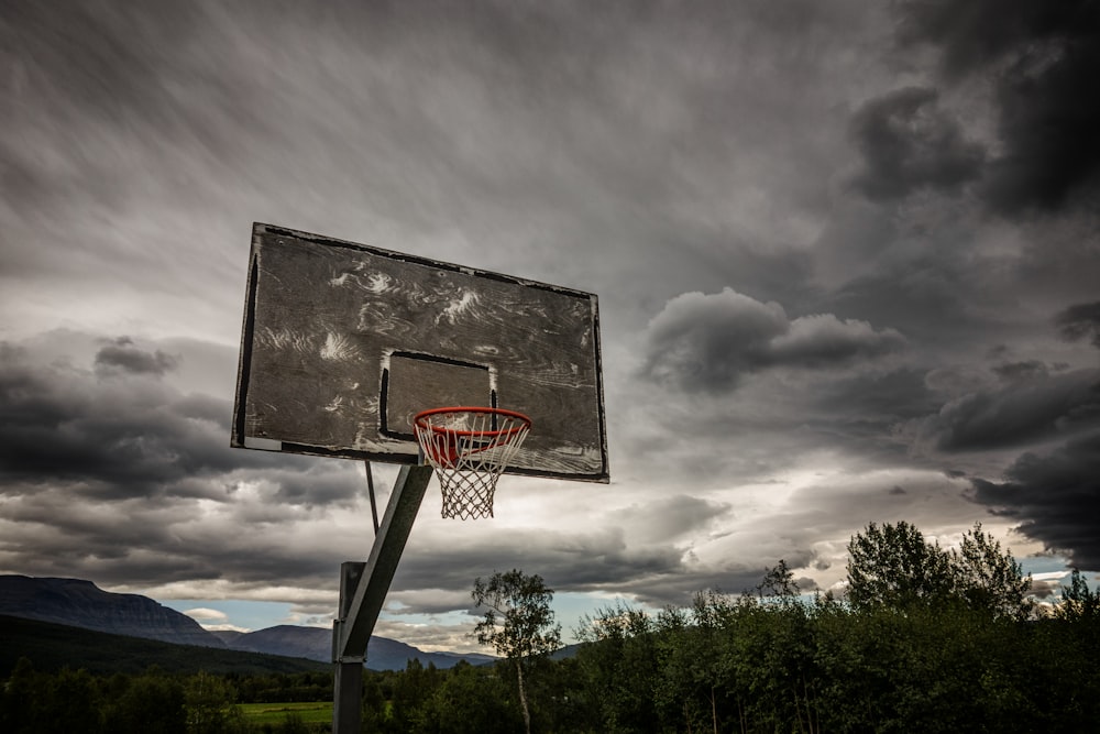 gray and white basketball hoop under dark clouds at daytime