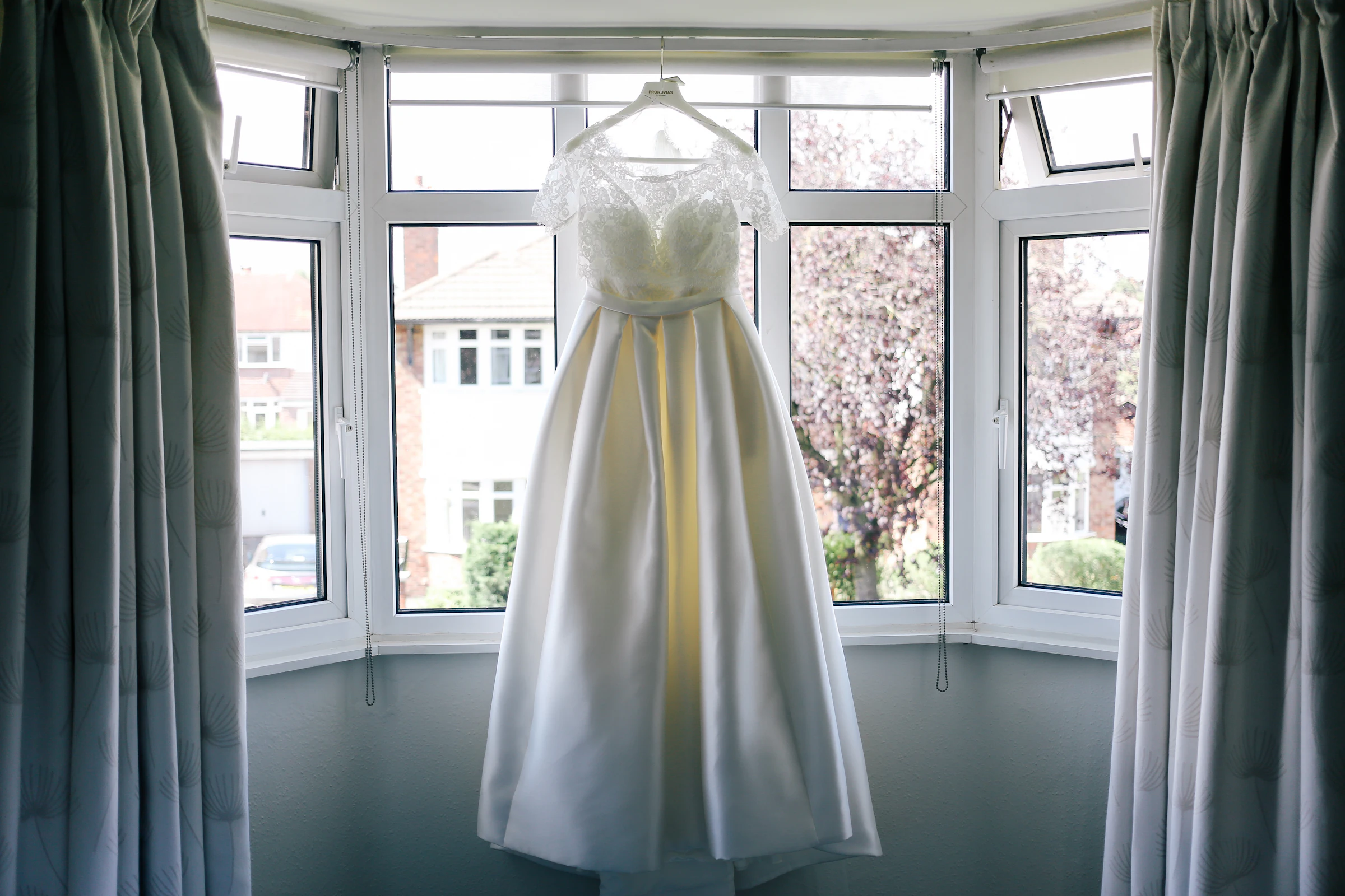 A wedding gown hanging in a bright bay window