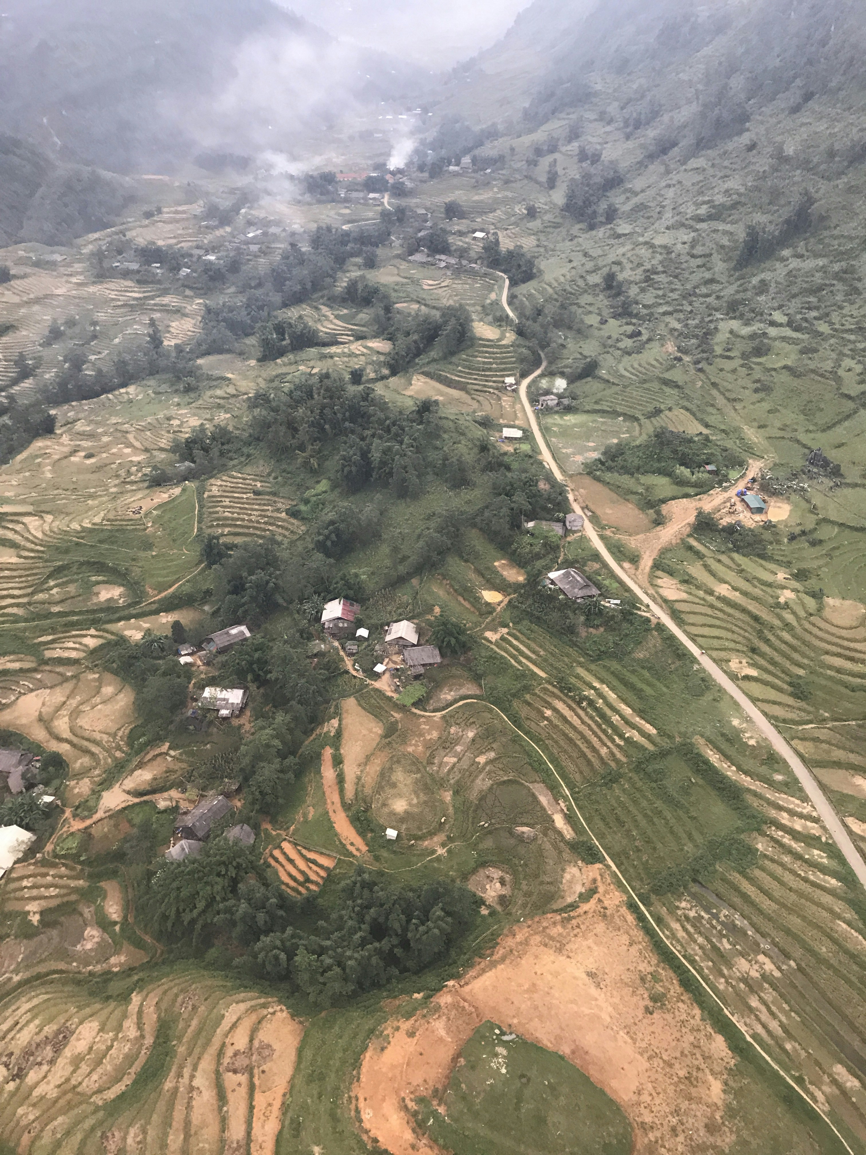 Aerial view of Bir Billing valley with green terraced fields, pine forests and Dhauladhar mountains in background, mist in valley