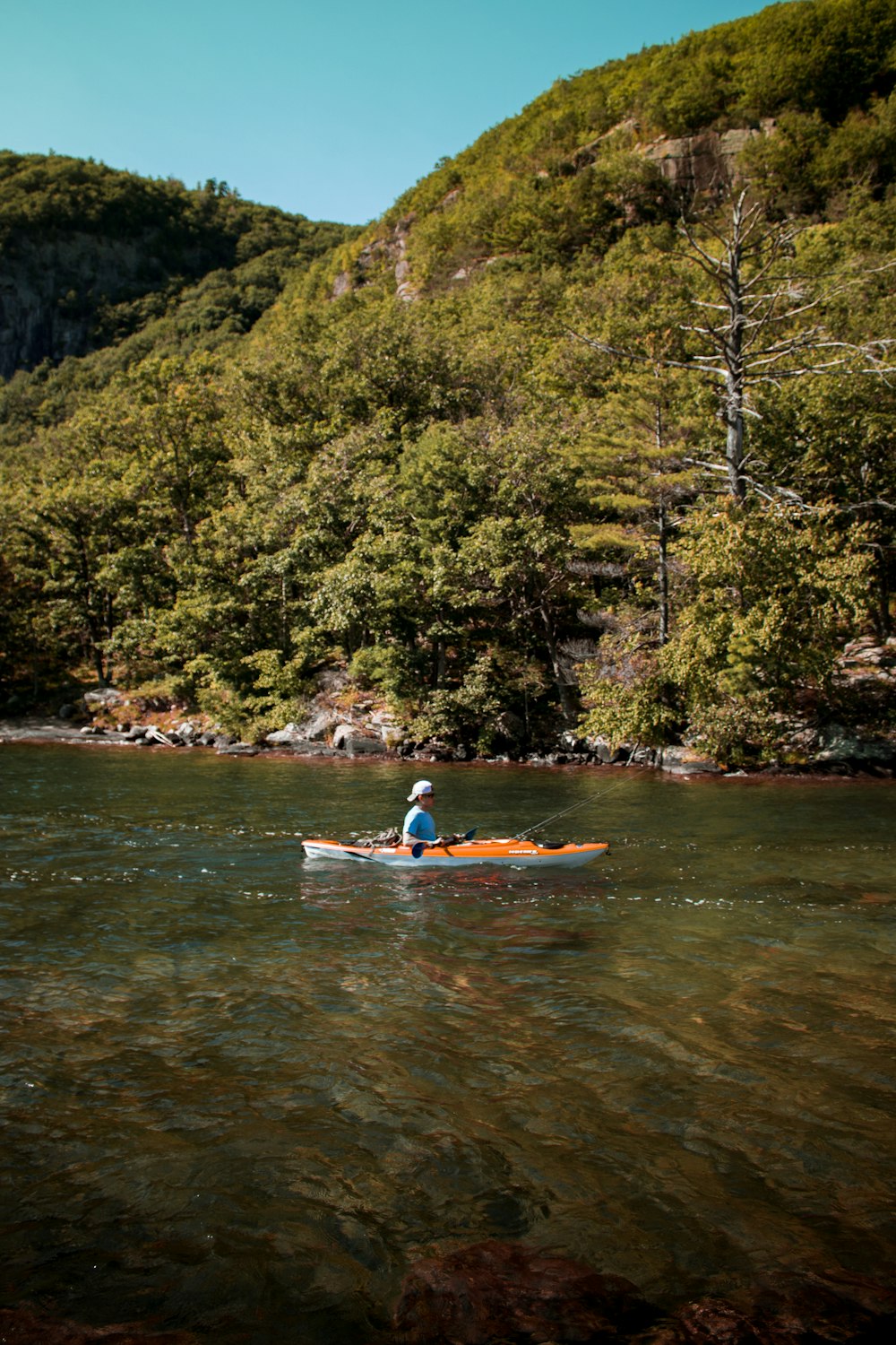 Hombre con camisa blanca montando kayak rojo en el río durante el día
