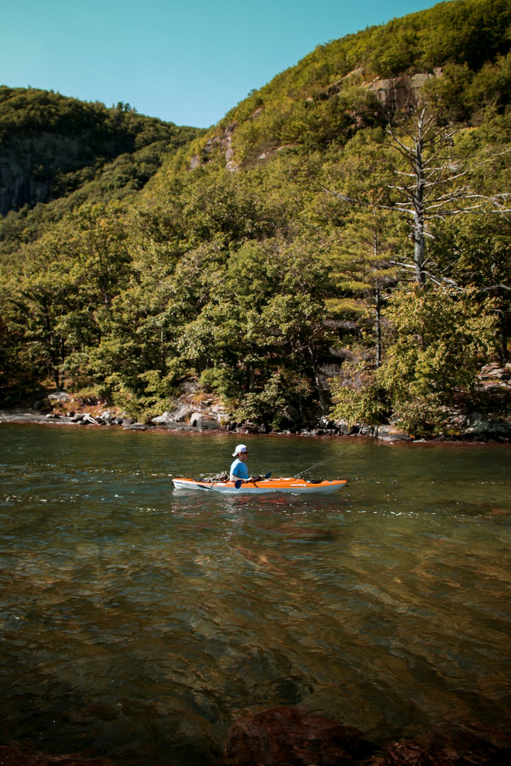 homme en chemise blanche équipant un kayak rouge sur la rivière pendant la journée