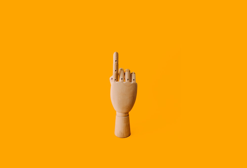 escultura de mão de madeira bege com fundo laranja