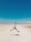 A person is captured mid-air while leaping across a barren, expansive desert landscape with mountains visible in the distance under a clear blue sky.
