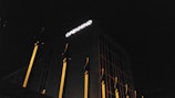 A building at night with a dark facade and a large white sign reading 'OPENMIND' illuminated on the upper section. The structure features several vertical golden-yellow elements resembling pillars or decorative fins against the dark background.