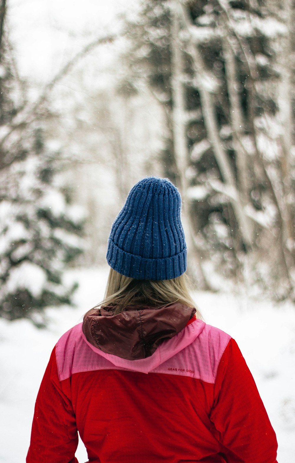 persona con gorra de punto y chaqueta con capucha roja y rosa mirando el árbol