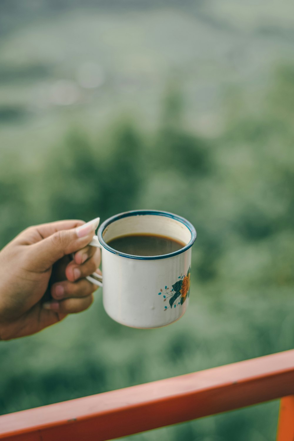 person holding white and orange floral mug